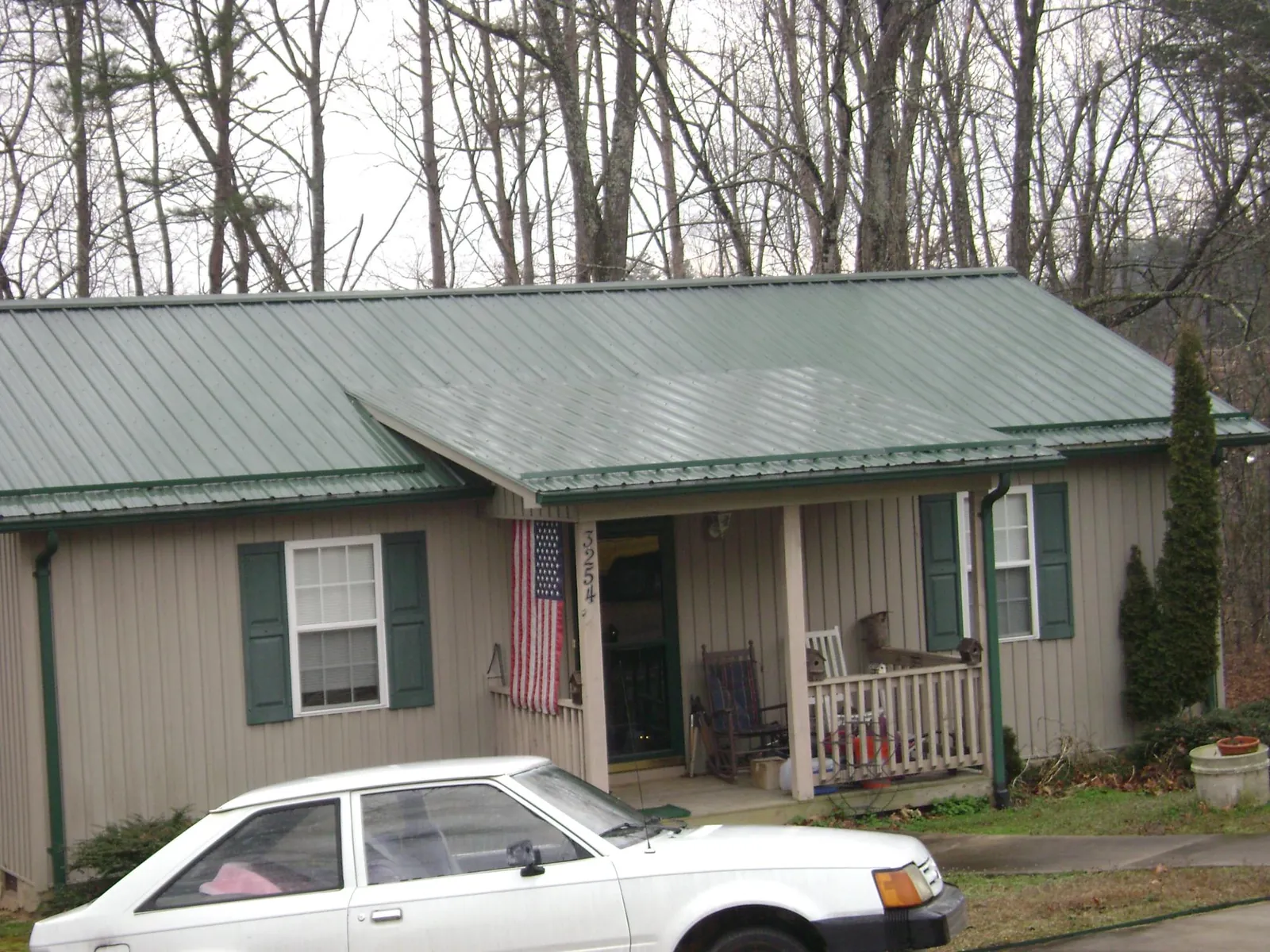 Green metal roof and front porch on a tan sided cottage in Lowell